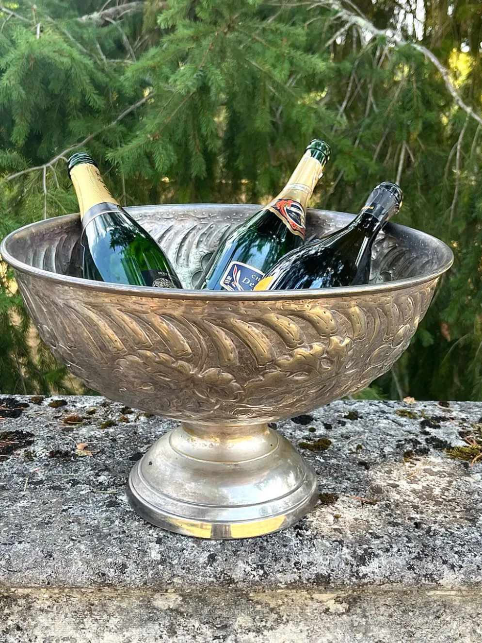 Seau à champagne en métal argenté sur piédestal avec des raisins.