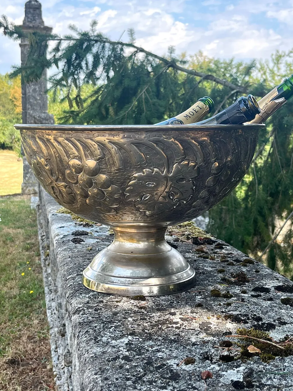 Seau à champagne en métal argenté sur piédestal avec des raisins.