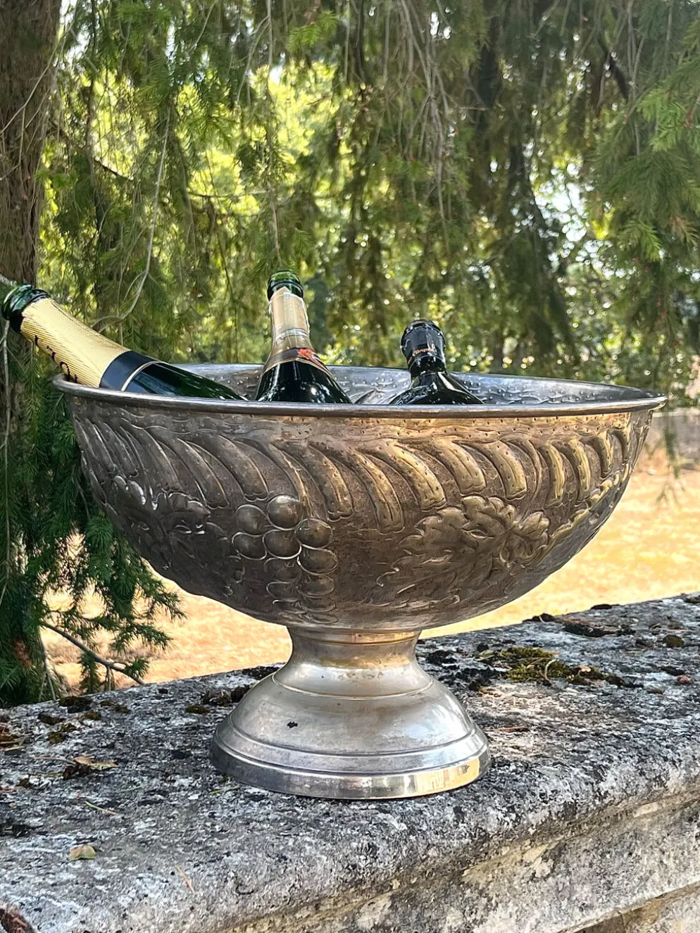 Seau à champagne en métal argenté sur piédestal avec des raisins.