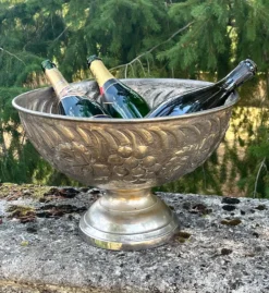 Seau à champagne en métal argenté sur piédestal avec des raisins.