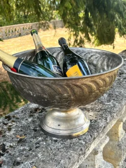 Seau à champagne en métal argenté sur piédestal avec des raisins.