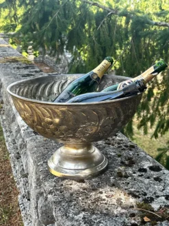 Seau à champagne en métal argenté sur piédestal avec des raisins.
