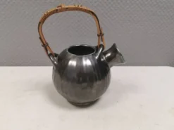 Une cruche en céramique avec un émail métallique et une poignée en raffia tressé.
