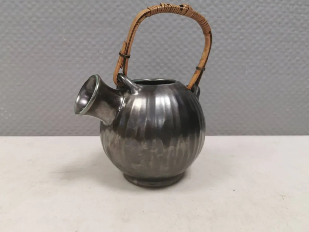 Une cruche en céramique avec un émail métallique et une poignée en raffia tressé.
