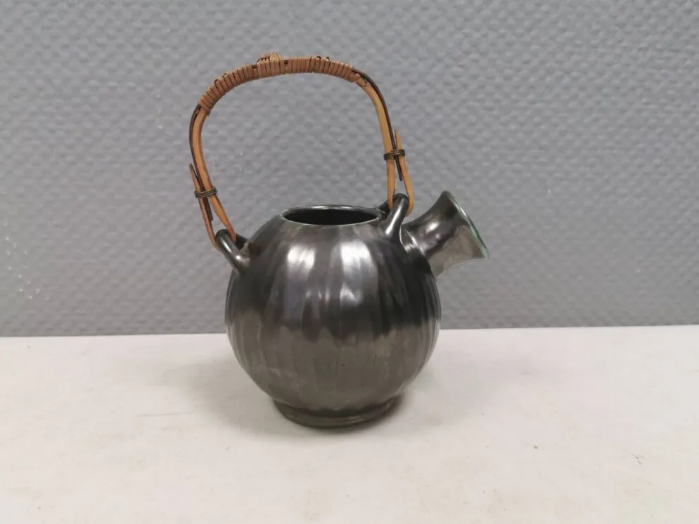 Une cruche en céramique avec un émail métallique et une poignée en raffia tressé.