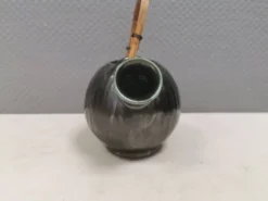 Une cruche en céramique avec un émail métallique et une poignée en raffia tressé.