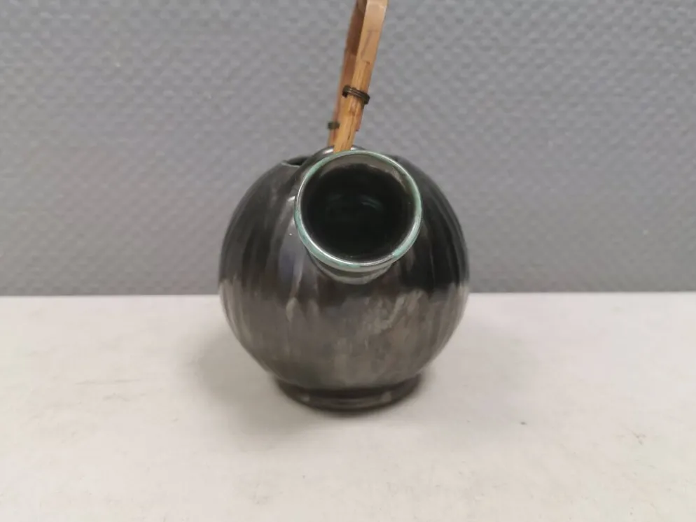 Une cruche en céramique avec un émail métallique et une poignée en raffia tressé.