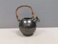 Une cruche en céramique avec un émail métallique et une poignée en raffia tressé.