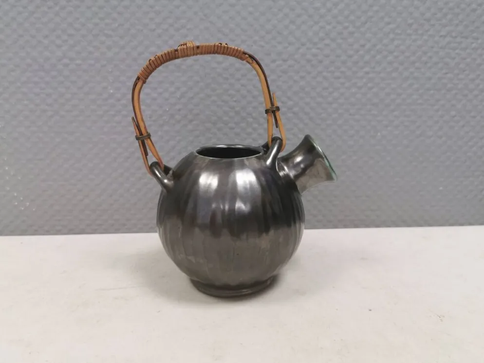 Une cruche en céramique avec un émail métallique et une poignée en raffia tressé.