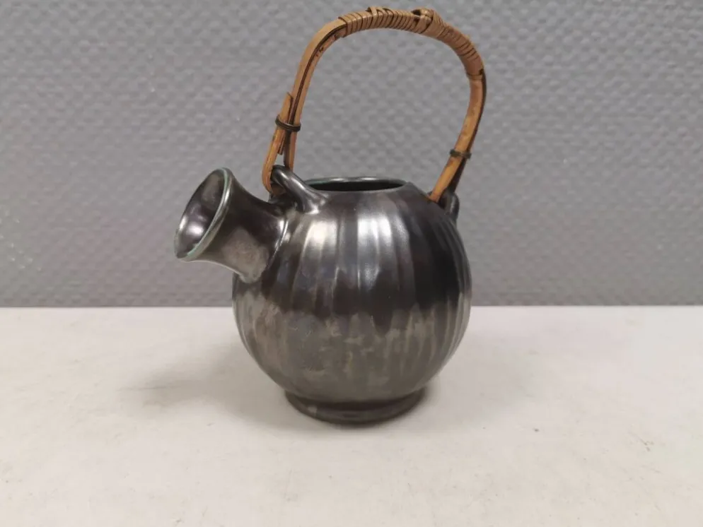Une cruche en céramique avec un émail métallique et une poignée en raffia tressé.