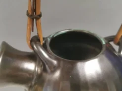 Une cruche en céramique avec un émail métallique et une poignée en raffia tressé.